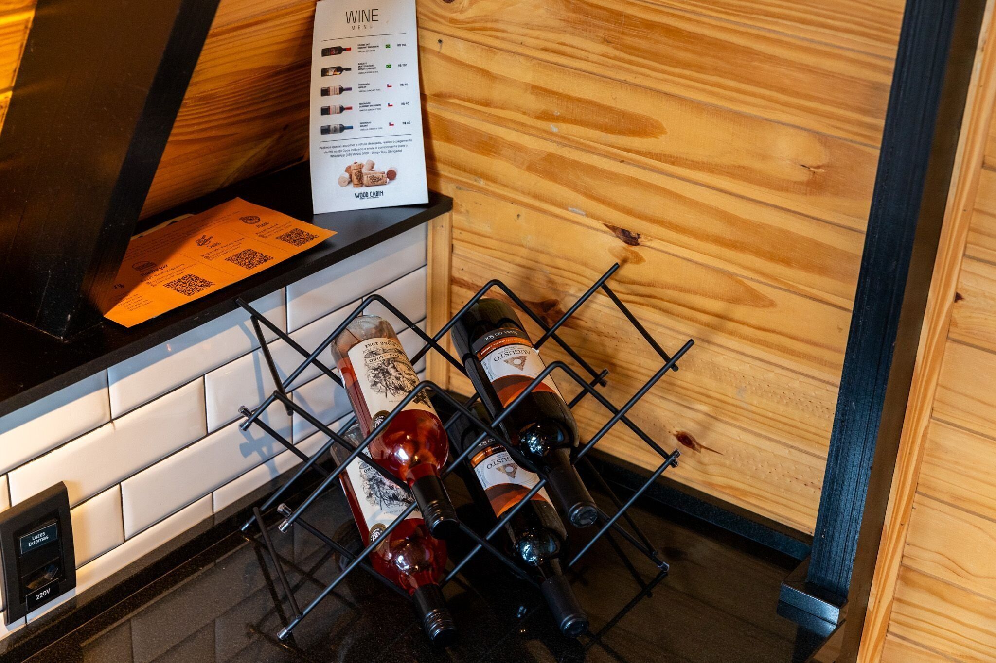 Una estantería con botellas de vino frente a una pared de madera, un menú sobre la encimera y un código QR en una servilleta.