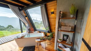 Ein modernes Badezimmer mit Badewanne, Holzboden und Blick auf eine üppige Landschaft.