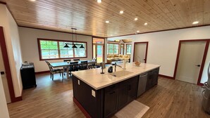 A spacious kitchen with a large island, wooden ceiling, and ample natural light from windows. - The Point House - Exclusive Lake Placid Boat-Access Home (Lake Placid)