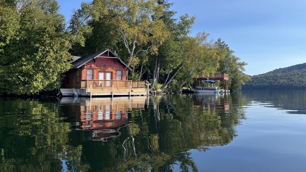 A cabin on stilts by a calm lake, surrounded by trees. - The Point House - Exclusive Lake Placid Boat-Access Home (Lake Placid)