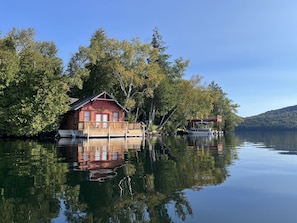 A cabin on stilts by a calm lake, surrounded by trees. - The Point House - Exclusive Lake Placid Boat-Access Home (Lake Placid)