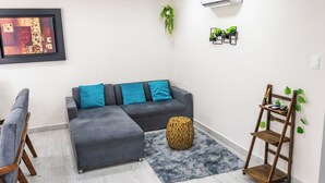 Un salon moderne avec un canapé d’angle gris, un petit tabouret rond en bois et un tapis gris à poils longs.