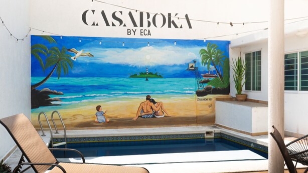 Une fresque représentant une scène de plage, avec le texte « CASABOKA BY ECA » au-dessus d’un espace piscine agrémenté de chaises longues.