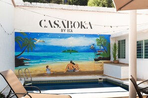 A mural of a beach scene with the text "CASABOKA BY ECA" above a swimming pool area with lounge chairs. - Casa Boka (Boca del Río)