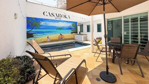 Un espace piscine avec des chaises longues et un parasol, une fresque représentant une scène de plage, et une enseigne indiquant « CASABOKA BY ECA ».