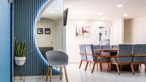 Un espace repas moderne avec un séparateur incurvé de couleur bleue, une plante en pot et une table à manger entourée de chaises à revêtement gris.