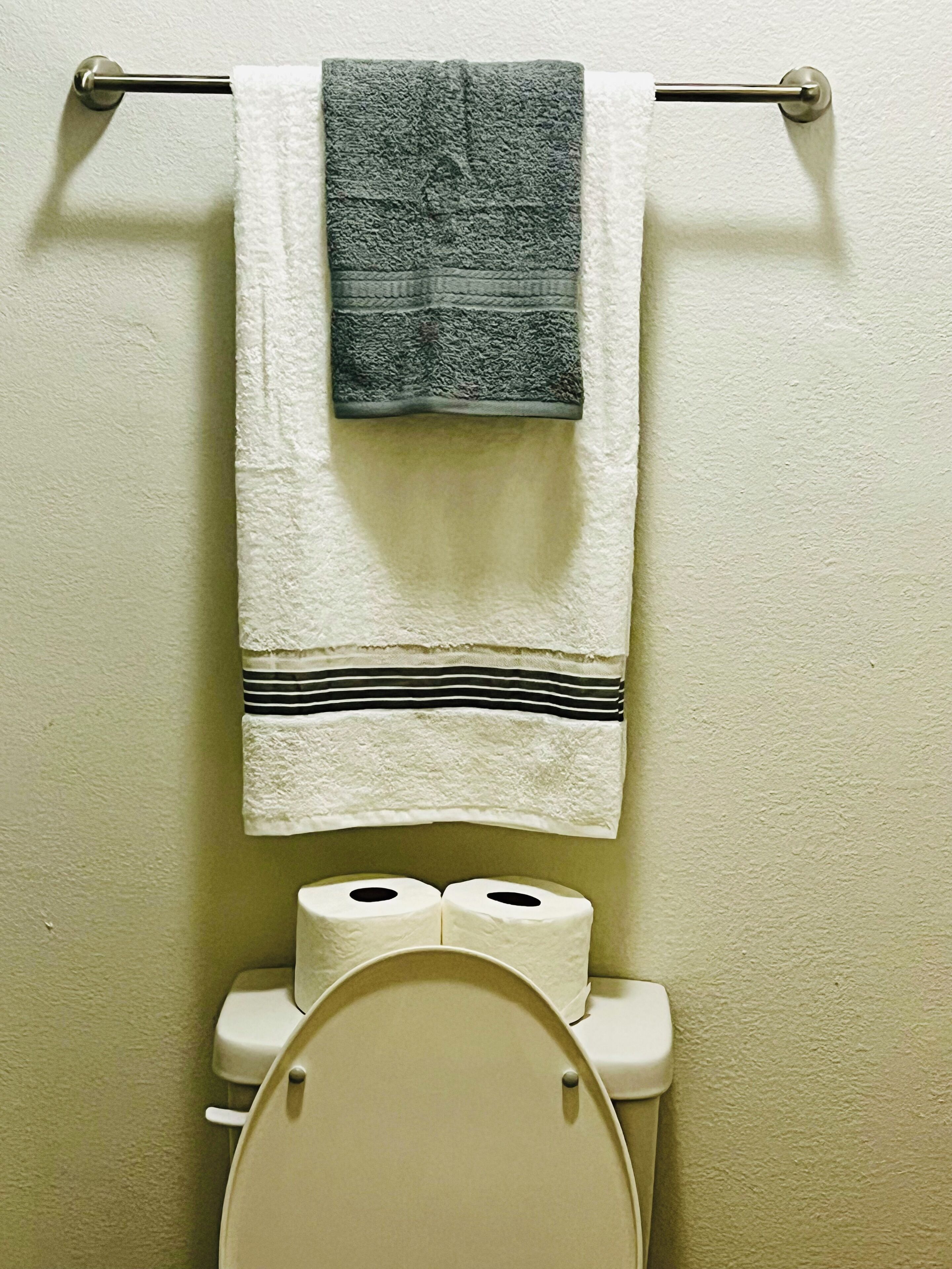 Un baño con inodoro, dos rollos de papel higiénico y un perchero con dos toallas.