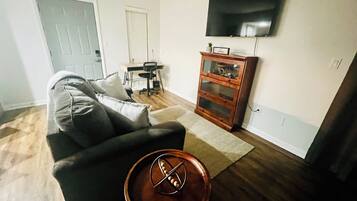 A living room with a sofa, a coffee table with a decorative item, a wooden cabinet, a television on the wall, and a door.