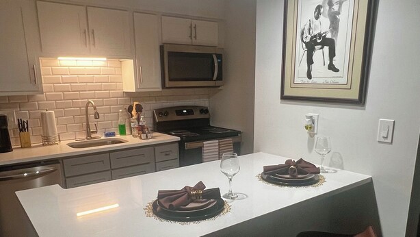 Une cuisine moderne avec des meubles blancs, un four à micro-ondes et un grand îlot central doté de tabourets de bar.