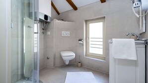 Une salle de bain moderne dotée d’une douche à parois de verre, de toilettes, d’un lavabo avec une serviette et d’une fenêtre laissant entrer la lumière naturelle.