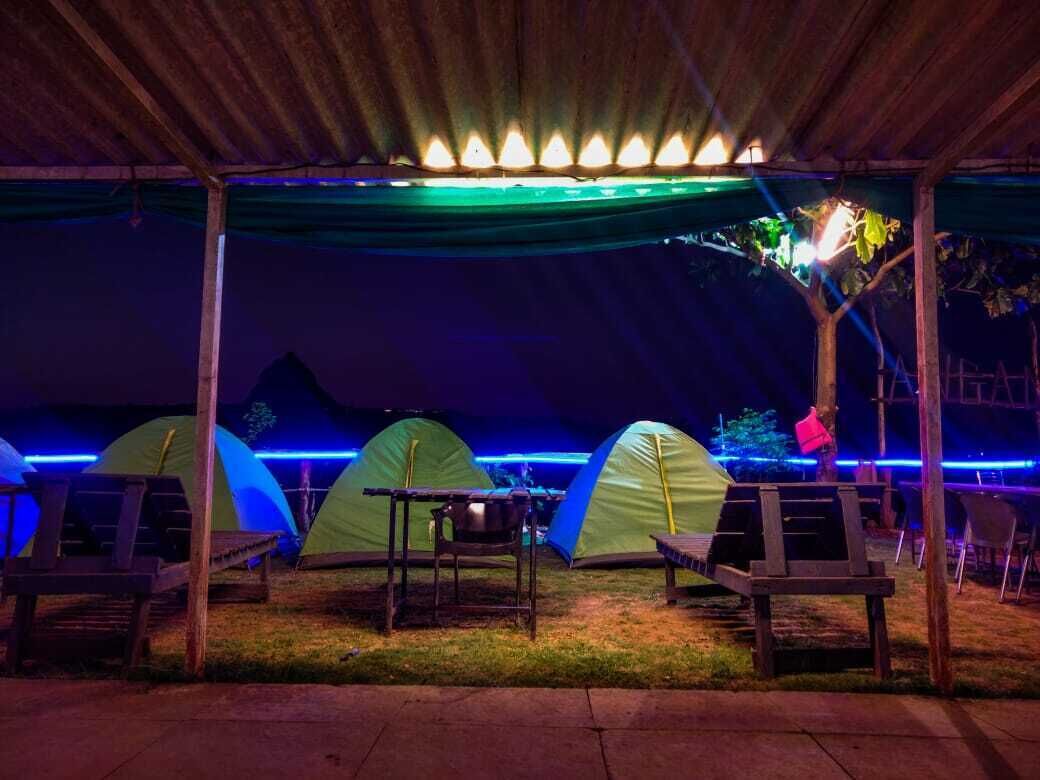 A covered outdoor area with multiple tents and benches, under a roof with lights.