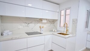 A modern kitchen with white cabinetry, a marble backsplash, and a gold faucet. - The Luxe Haven (Cerdanyola del Vallès)