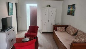 A room with a television on a white cabinet, a red armchair, a wooden bed with floral pillows, and a white wardrobe with decorative leaf patterns. - Getaway for two: cosy apartment with balcony (Trouville-sur-Mer)