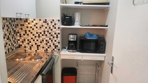 A compact kitchen with a stove, microwave, coffee maker, and a small trash bin. - Getaway for two: cosy apartment with balcony (Trouville-sur-Mer)
