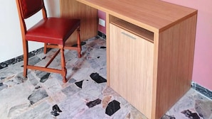 A corner room with a wooden desk and a red chair, a tiled floor, and a pink wall.