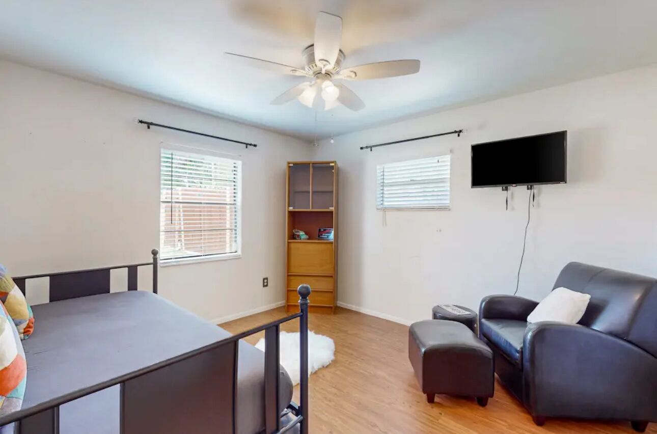 A living room with a ceiling fan, a TV mounted on the wall, a sofa, a small table, and a wooden cabinet.