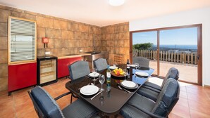 A dining area with a table set for four, a kitchen area with a red cabinet, and a view of the sea through a large sliding glass door. - Villa Asomada - Four Bedroom Villa, Sleeps 8 (La Asomada)