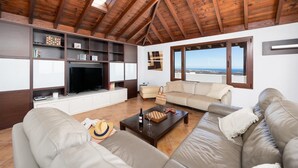 A spacious living room with a high ceiling, built-in wooden shelves, a large flat-screen TV, and a comfortable seating area with a view of the sea. - Villa Asomada - Four Bedroom Villa, Sleeps 8 (La Asomada)
