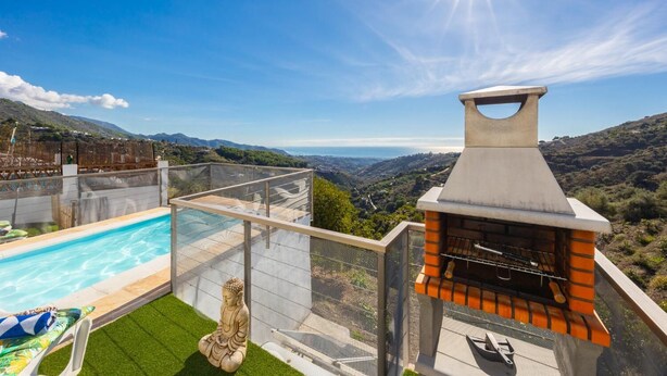 A pool with a Buddha statue, a barbecue grill, and a scenic view of hills and a body of water.