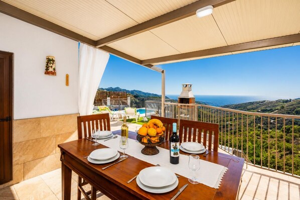Une table dressée pour un dîner à deux, avec des assiettes, des couverts, une bouteille de vin et un panier de fruits.