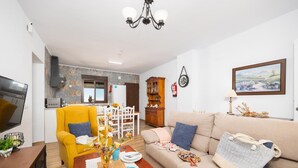 A modern living room with a yellow armchair, beige sofa, and a dining area with a wooden table and chairs.