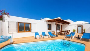 Una piscina con agua azul, rodeada de sillas de descanso azules y una pérgola de madera.
