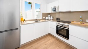 Una cocina moderna con gabinetes blancos, un refrigerador de acero inoxidable, un microondas, una cafetera y un horno.