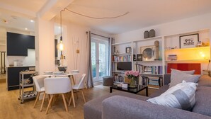 A modern living room with a grey sofa, a coffee table, and a bookshelf. There is a dining area with a table and chairs, and a kitchen in the background. - Host Stay Osbourne Rest (Hove)