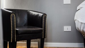 A black leather chair with gold studs, positioned against a grey wall with a white switch plate. - Emilia Suite Academy (Modena)