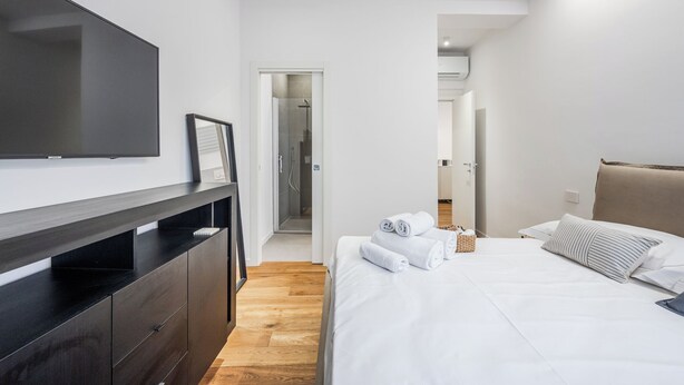 A modern hotel room with a large flat-screen TV, a wooden floor, a bed with white linens, and a dark wooden dresser. - Emilia Suite Academy (Modena)
