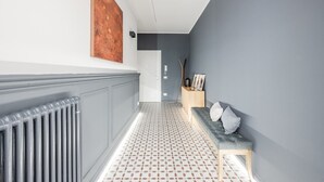 A hallway with a radiator, a patterned floor, a grey bench with cushions, a wooden sideboard, and a large abstract painting on the wall. - Emilia Suite Academy (Modena)