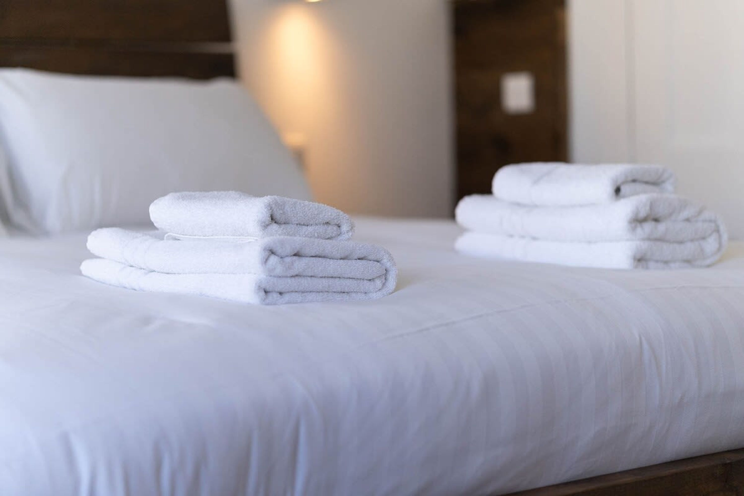 A neatly made bed with folded white towels and a wooden headboard.