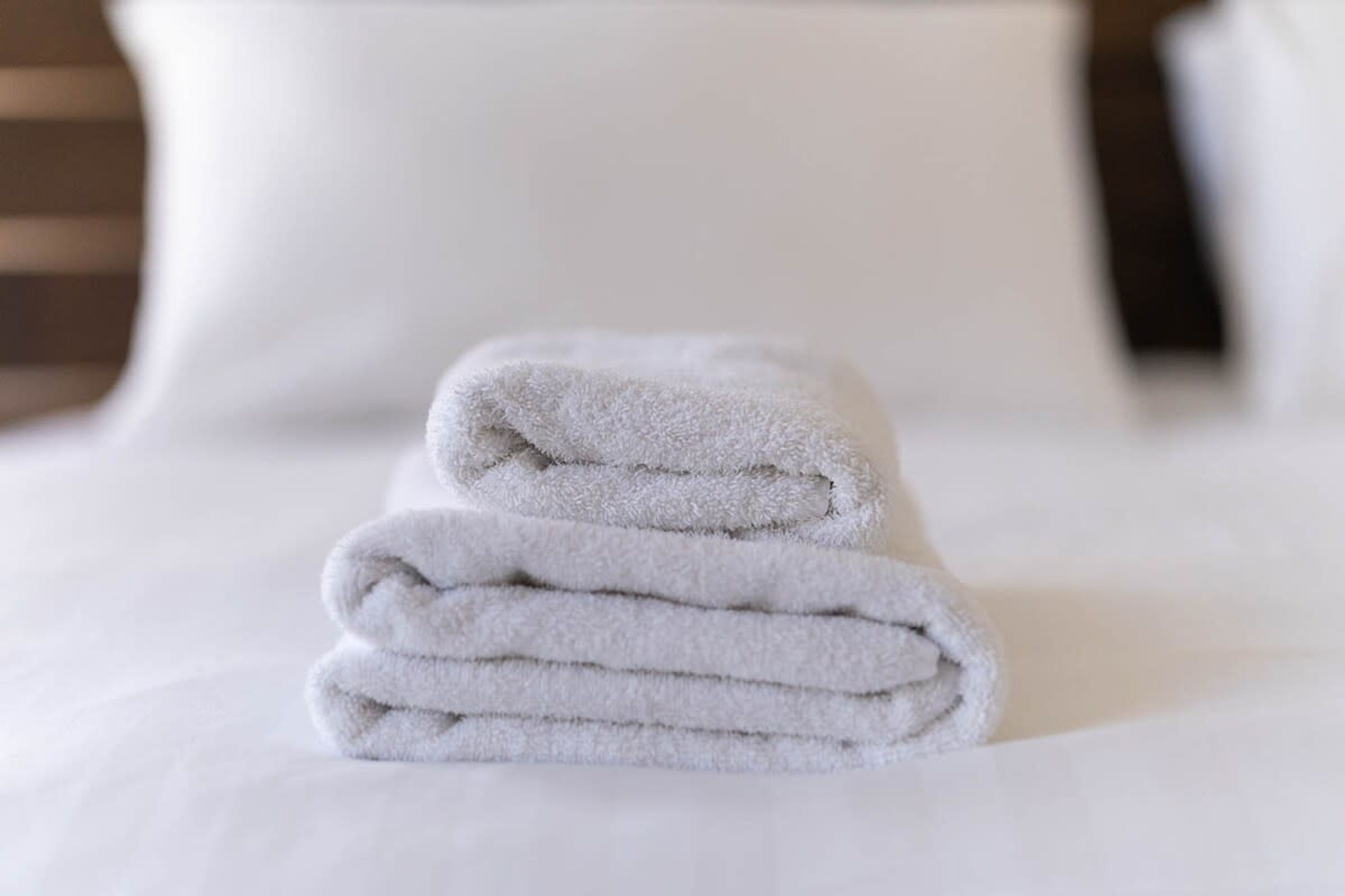 Een stapel witte handdoeken op een bed met witte lakens.