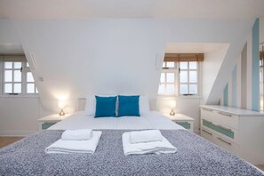 Une chambre à coucher avec un grand lit, deux tables de chevet, une commode et une fenêtre avec des stores.
