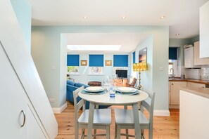 A dining area with a round table set for two, a blue sofa in the background, and a kitchen visible through an open doorway. - Host Stay Blue Bolthole on Vicarage Lane (Brighton)