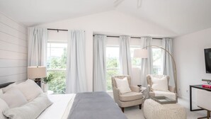 Ett modernt hotellrum med en stor säng, två fåtöljer, ett litet bord och en TV.