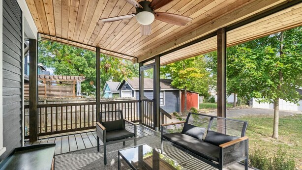 Ein überdachter Außenbereich zum Sitzen mit Deckenventilator, Holzdeck und Blick auf die Nachbarschaft.