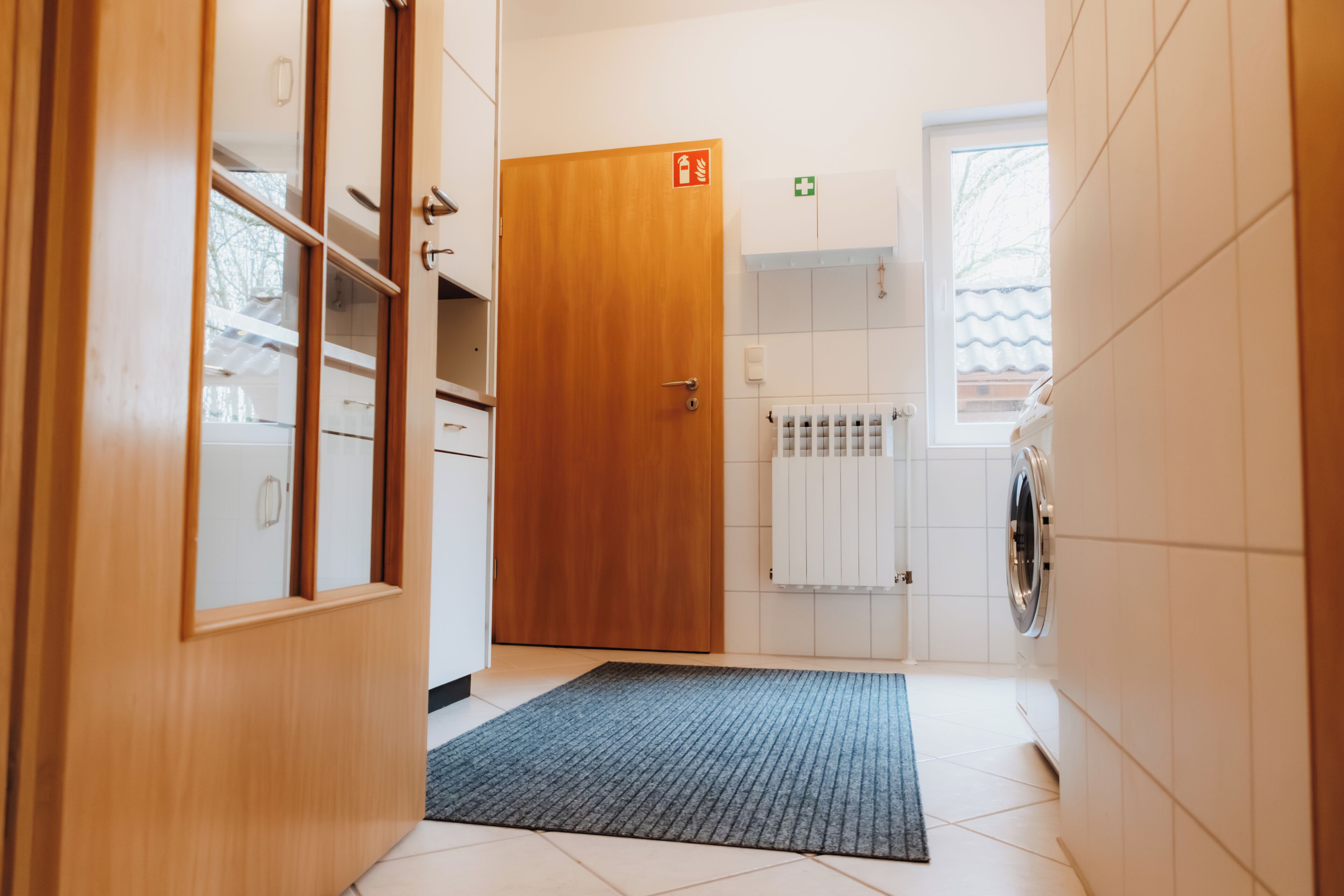 A hotel room with a wooden door, a radiator, a washing machine, and a small window.