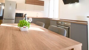 Un'area pranzo con un tavolo in legno, sedie, una pianta in vaso e una cucina sullo sfondo.