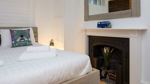 A neatly made bed with white linens, a colorful pillow, a small blue toy car on the mantel, and a fireplace with a plant beside it. - Host Stay Grafton Driftwood (Brighton)