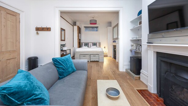 A modern living room with a grey sofa, teal cushions, a fireplace, and a kitchen area in the background. - Host Stay Grafton Driftwood (Brighton)