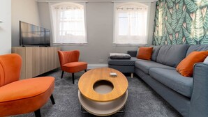 A modern living room with a sofa, two armchairs, a coffee table, a TV, and a patterned wall. - Host Stay Portland Apartment (Brighton)