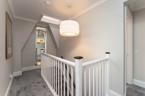 Stylish staircase leads to an upper level, flanked by light grey walls and a textured pendant light.