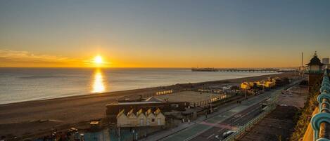 A coastal road with a sunset, a beach, and a bridge in the distance.