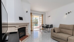 A living room with a fireplace, a sofa, a TV, and a dining area with chairs and a table. - Ory Red Apartment, São Rafael, Albufeira (Albufeira)