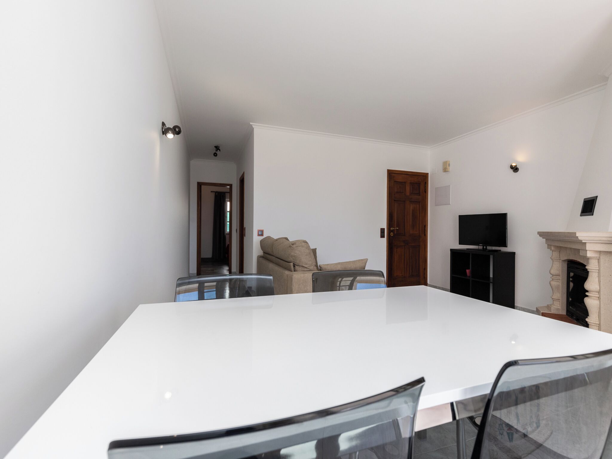 Ein modernes Wohnzimmer mit einem weißen Esstisch, einem beigefarbenen Sofa, einem Fernseher und einem Kamin.