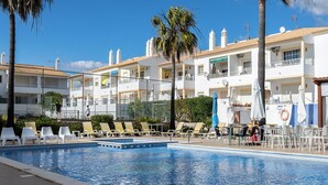 A swimming pool with lounge chairs and umbrellas, surrounded by multi-story buildings with balconies. - Ory Red Apartment, São Rafael, Albufeira (Albufeira)