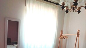 A hotel room with a bed, a hanging light fixture, a mirror, and a window with curtains. - Sassari Torres Rooms 2 (Sassari)
