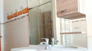 A bathroom with a white sink, wooden cabinets, a glass shower enclosure, and a mirror. - Sassari Torres Rooms 2 (Sassari)