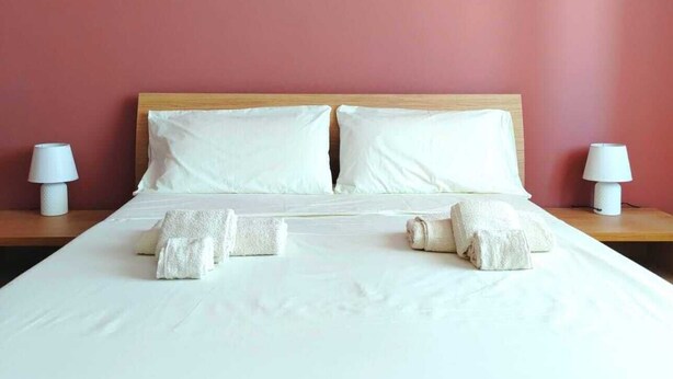 A neatly made bed with white linens and pillows, two bedside lamps, and a wooden headboard. - Sassari Torres Rooms 2 (Sassari)
